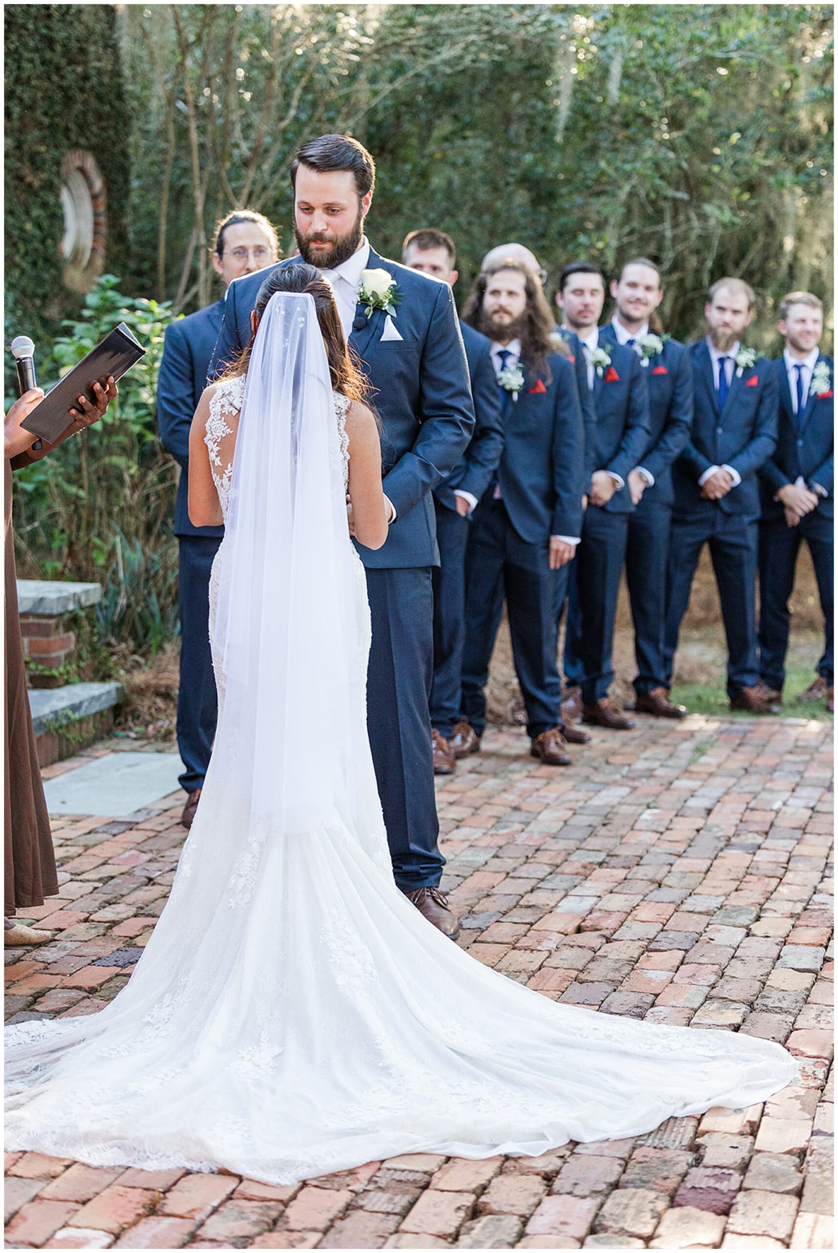 Newlyweds exchange vows with the groomsmen looking on behind them on a brick path at south eden plantation