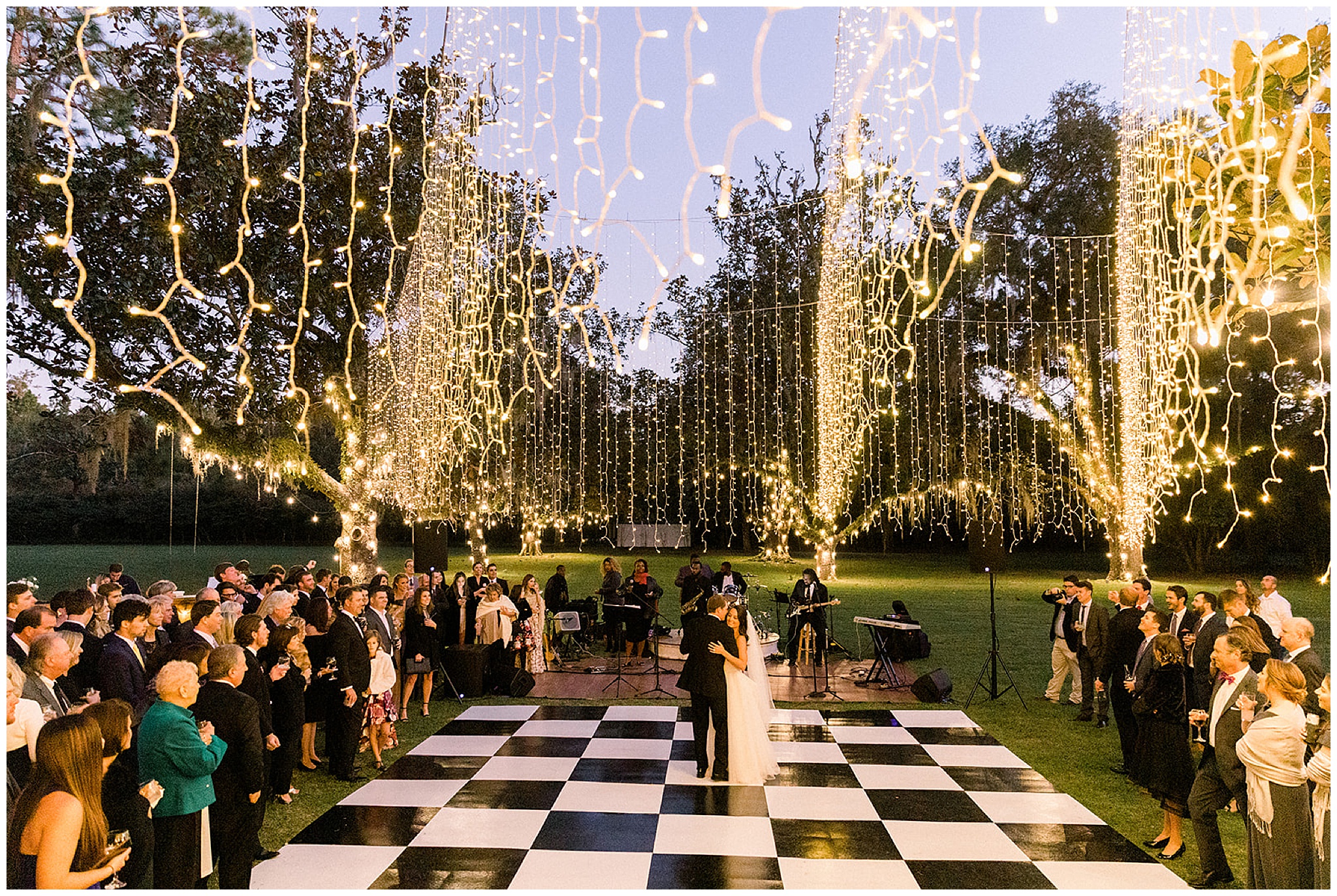 Newlyweds dance on an outdoor checkered dance floor under dangling string lights with their guests all watching at the south eden plantation