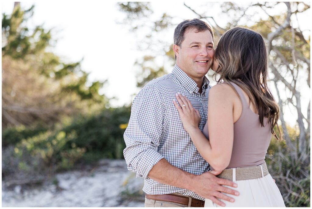 Bride-to-be in white dress embracing fiancé during golden hour at Mashes Sands Beach, a popular engagement location near Tallahassee