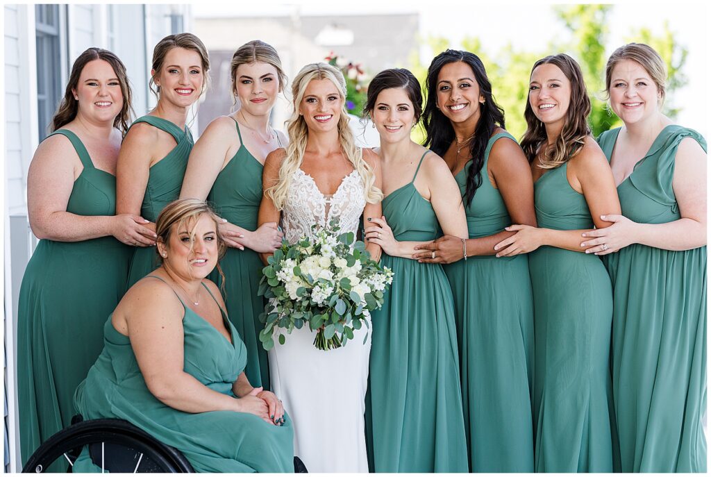 Bride surrounded by bridesmaids in green dresses holding white and green bouquets at coastal North Florida wedding