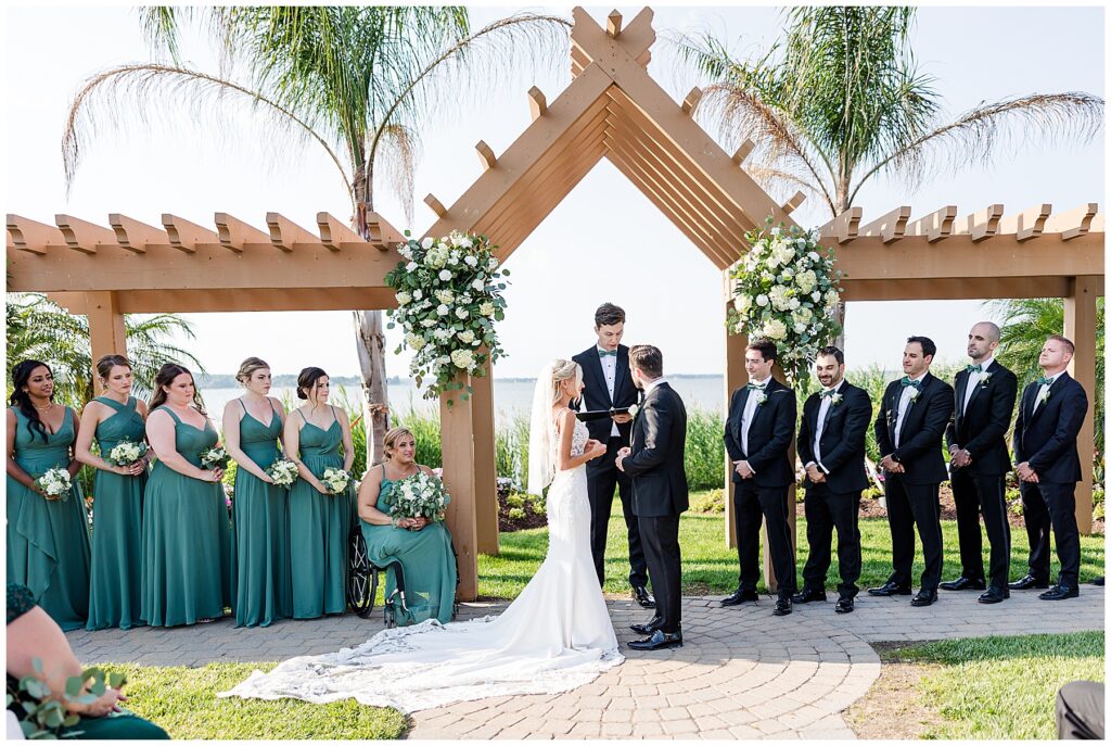 Bride and groom standing with bridesmaids in green dresses and groomsmen at coastal North Florida wedding ceremony