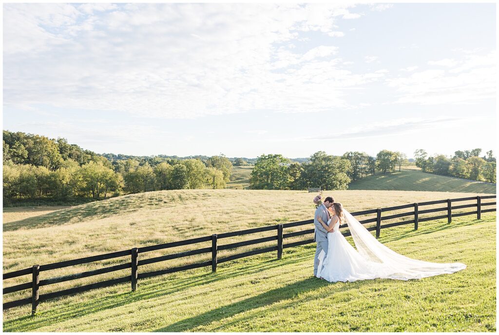 Smiling bride and groom walk hand in hand across a grassy pasture at their North Florida barn wedding.