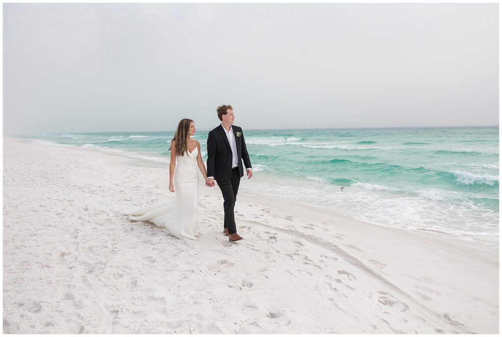 Audrey and Thomas walking hand in hand on the foggy Santa Rosa Beach shoreline.