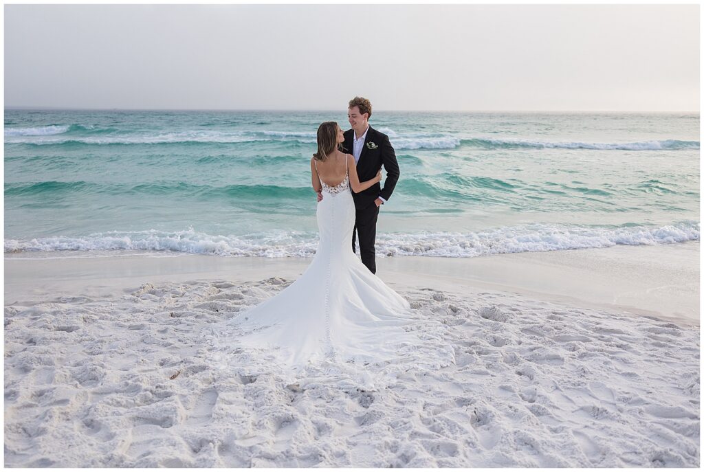 Wide coastal portrait showing the couple framed by sunset and shoreline on 30A.